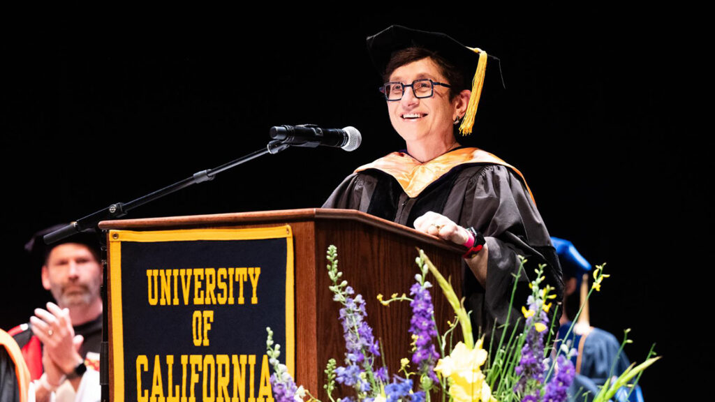 Gigi Sohn, wearing a cap and gown, gives a speech as a podium