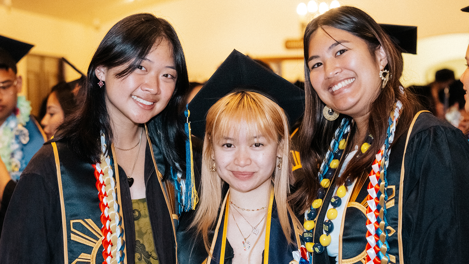 three Pilipinx graduates in gowns pose together