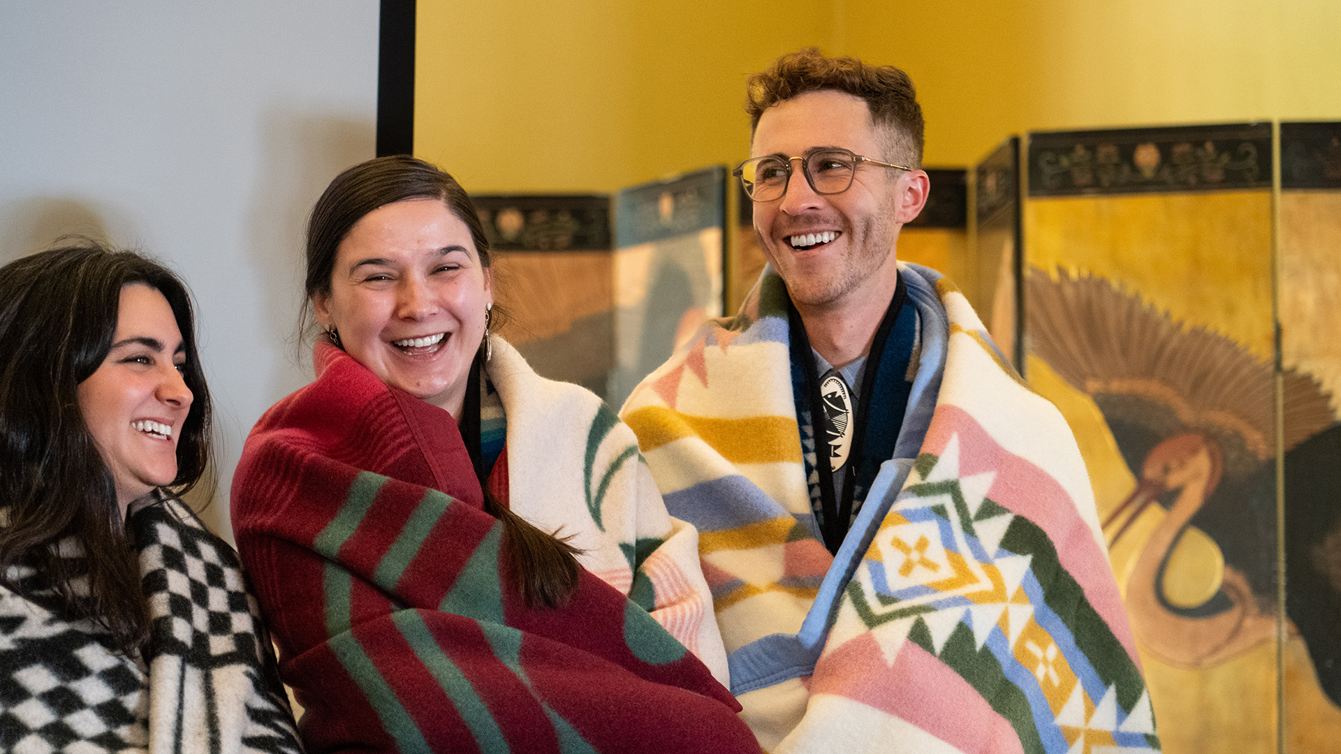 Three Native law graduates stand and laugh together with their new Native blankets