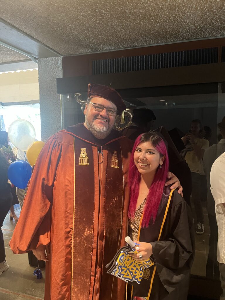 Pablo Gonzalez wearing a faculty graduation robe standing next to Ceclie Lopez during her graduation.