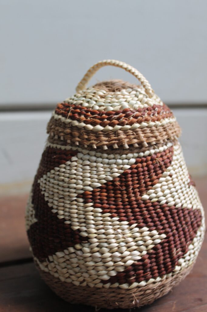 a close-up photo of a small, handwoven basket with red and white arrows wrapping around the body of the basket