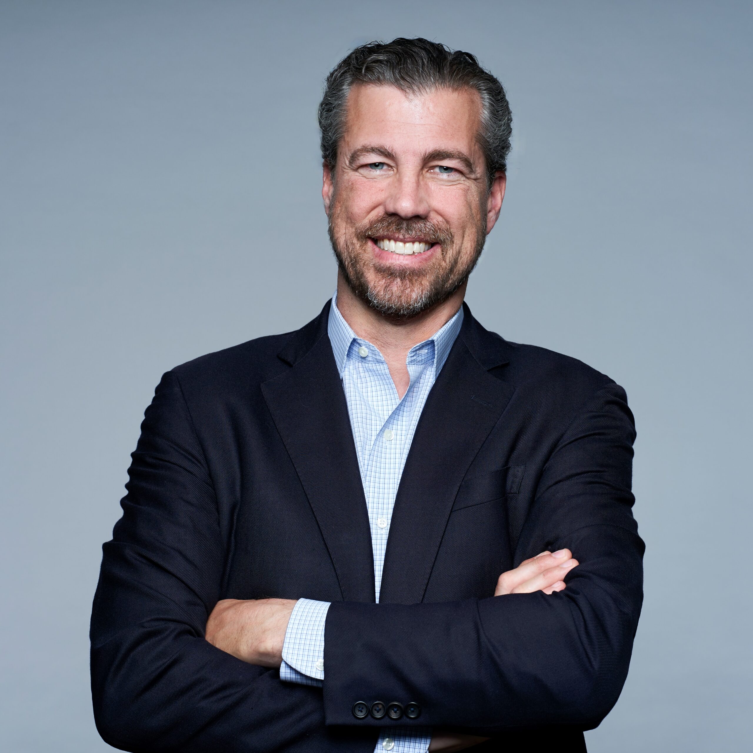 Darren Cooke wearing a suit and smiling with his arms folded.