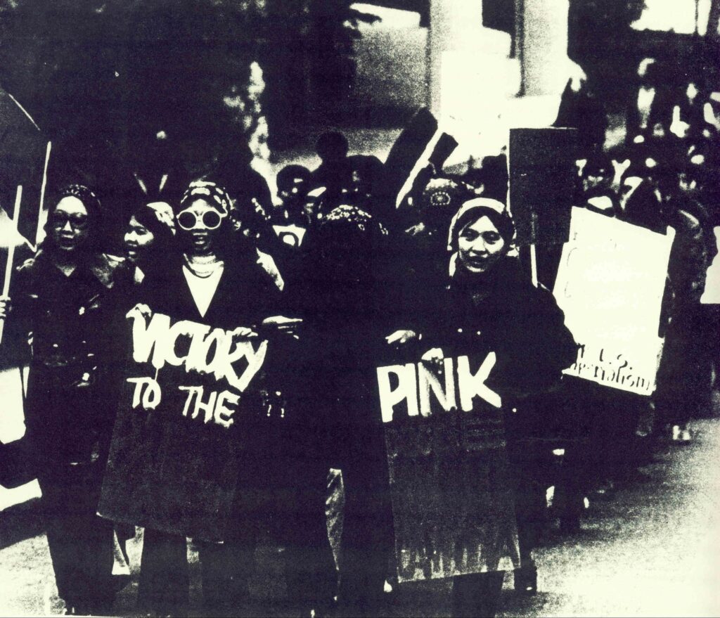 Victoria Wong holds a "victory to the pink" sign as she walks with other activists on the street.