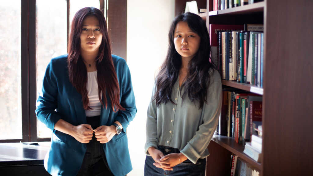 Students Madeleine Wong (left) and Melinda Zou stand in room next to a bookshelf. _2024_edit