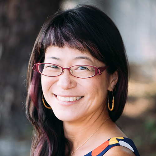 headshot of a person with long dark hair and glasses smiling