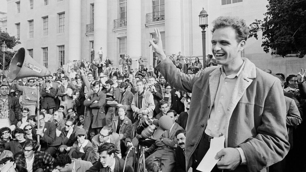 Mario Savio, a leader of the Free Speech Movement in 1960s Berkeley, flashes a peace sign with hundreds of students on the steps behind him on the steps of Sproul Hall.