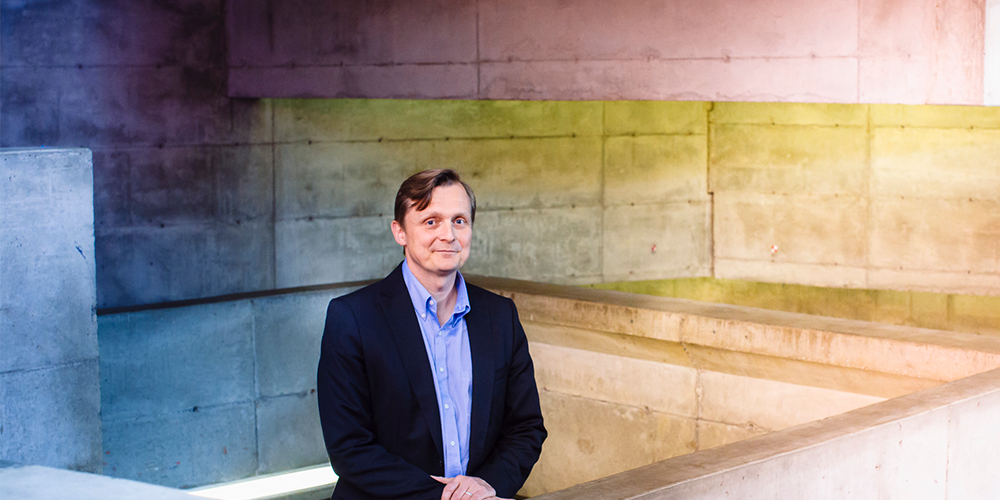 man in dark blue coat and blue shirt standing in front of pastel illuminated concrete walls