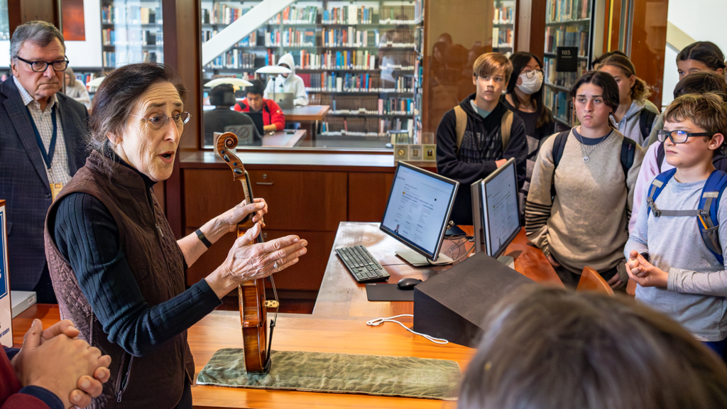Carla Shapreau holds and talks about an old and precious viola to a small group of middle school students 