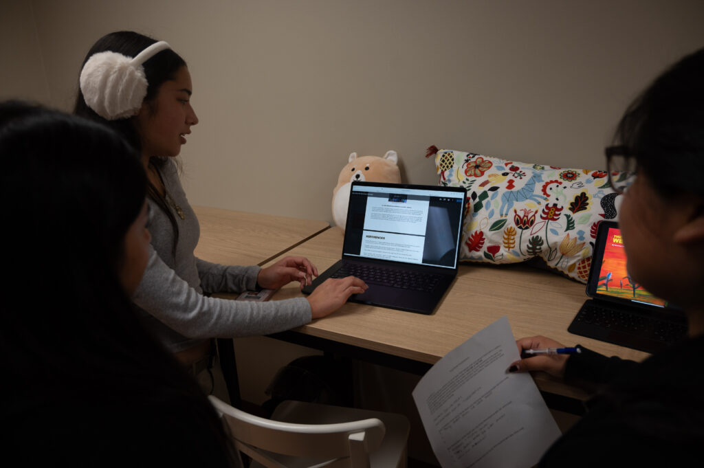 Poinciana Hung Haas sits with two other students and presents a document on her lap top.