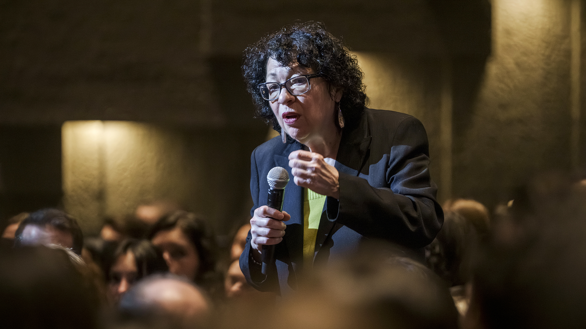 Sonia Sotomayor stands among audience members sitting in an auditorium while giving a lecture