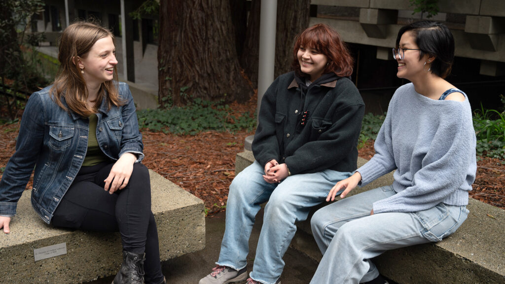 Mirin, Lee and Amy sit on benches in a campus courtyard and chat
