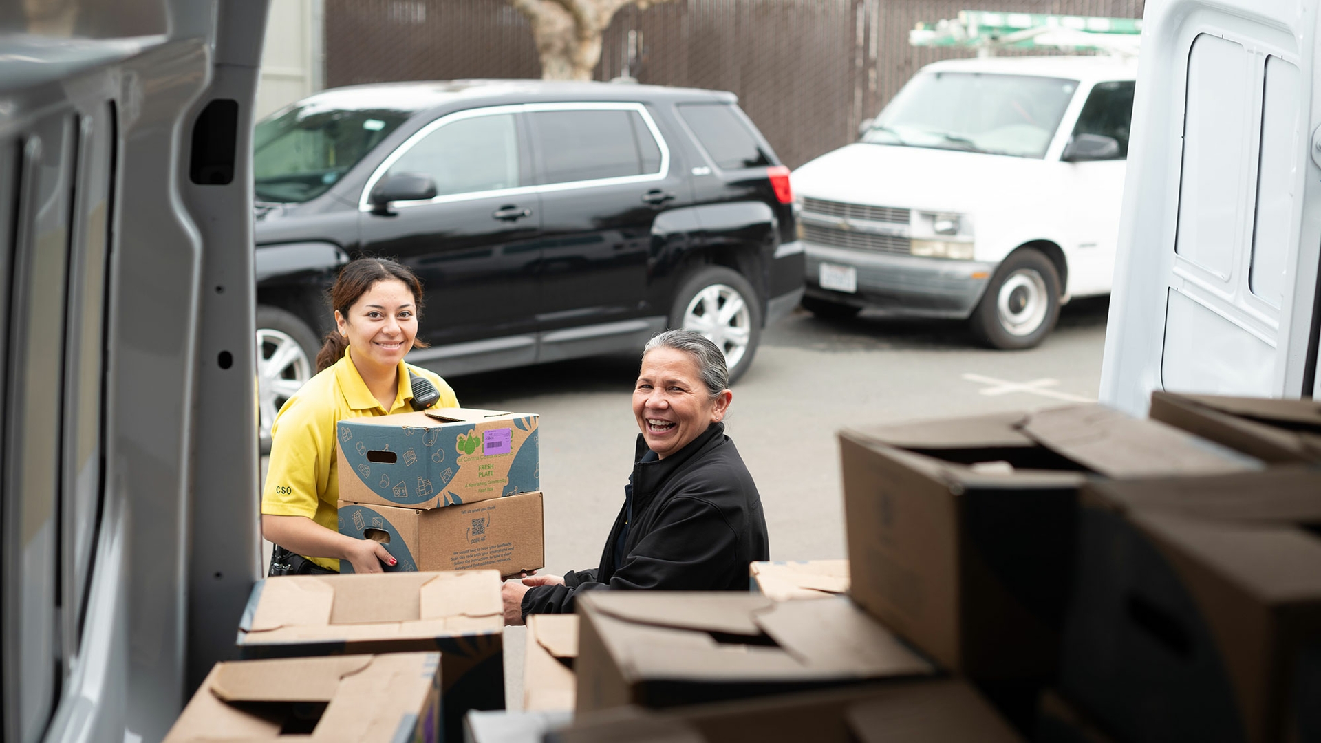 A photo shows two smiling people unloading boxes from the back of a van.