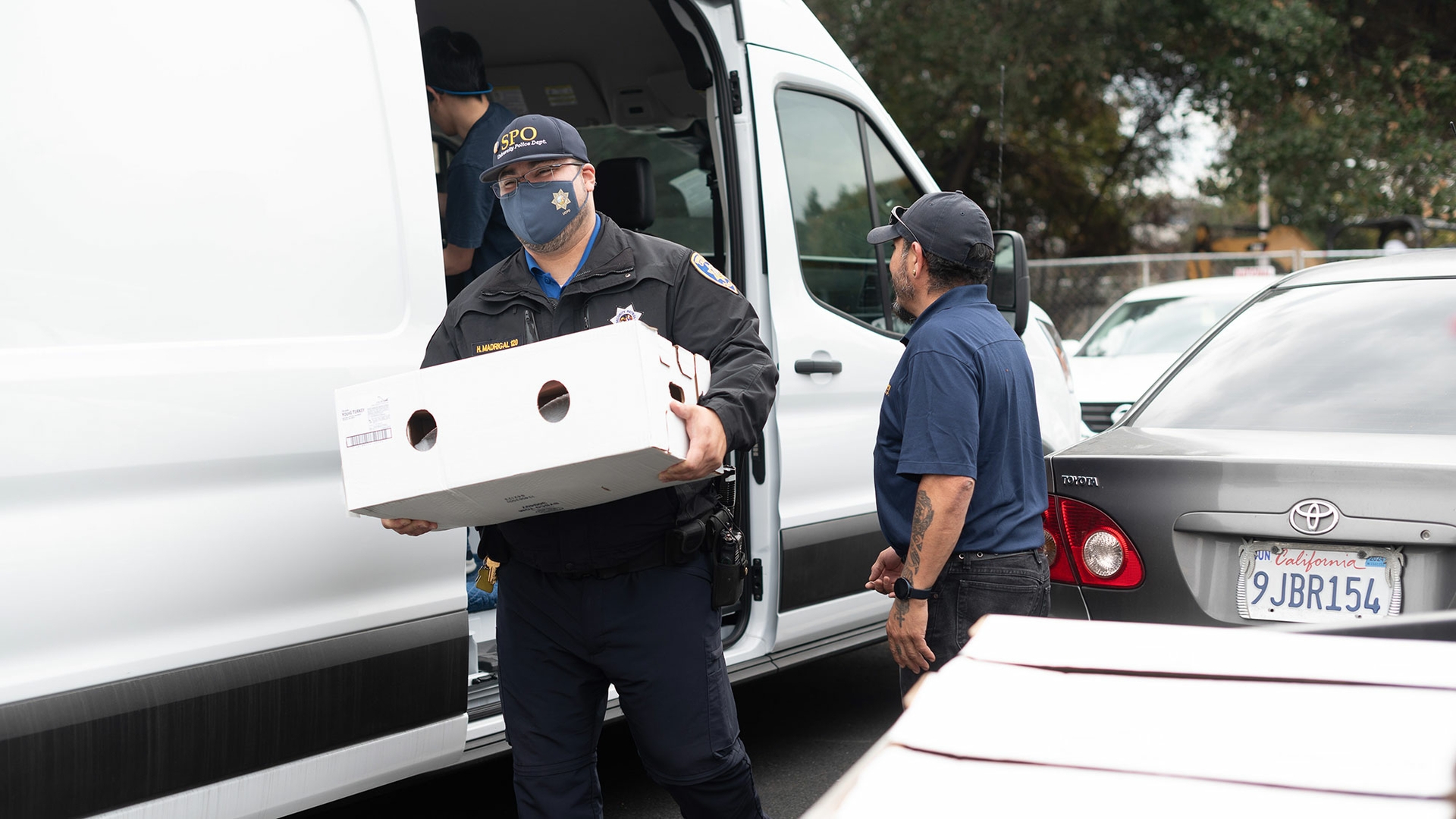 A volunteer wearing a police uniform unloads a box from a white van.