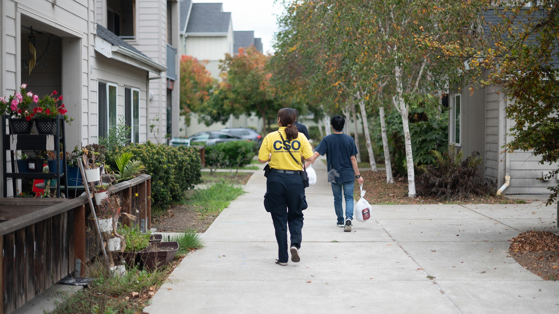 A volunteer wearing a yellow shirt and black pants walks through University Village.