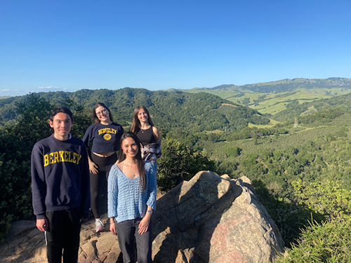 Four students who work with Professor Nicole Starosielski stand together on a large rock with rolling hills in the background.