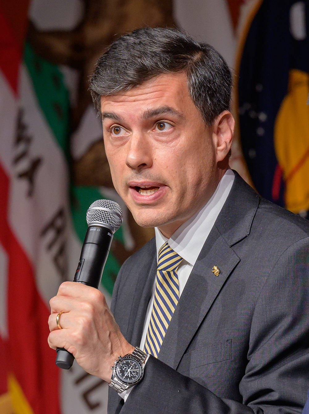 man in suit holding microphone, California flag in background