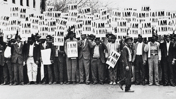At a 1957 civil rights protest, scores of Black men in a black & white photo carry signs reading "I Am a Man"