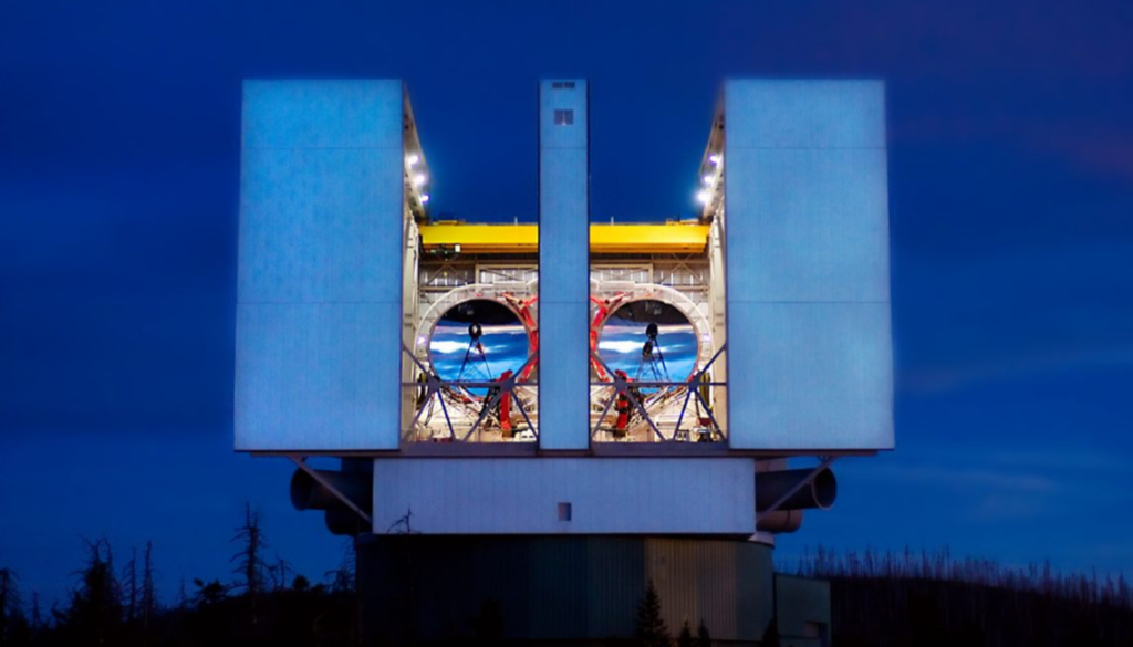 twin mirrors peak out from a telescope against a dim blue sky