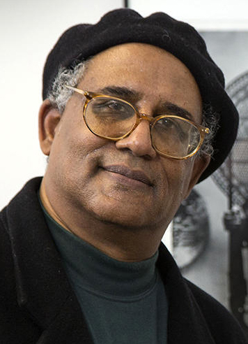 Waldo Martin wears a black beret posing in front of a photograph of Black Panther leader Huey P. Newton