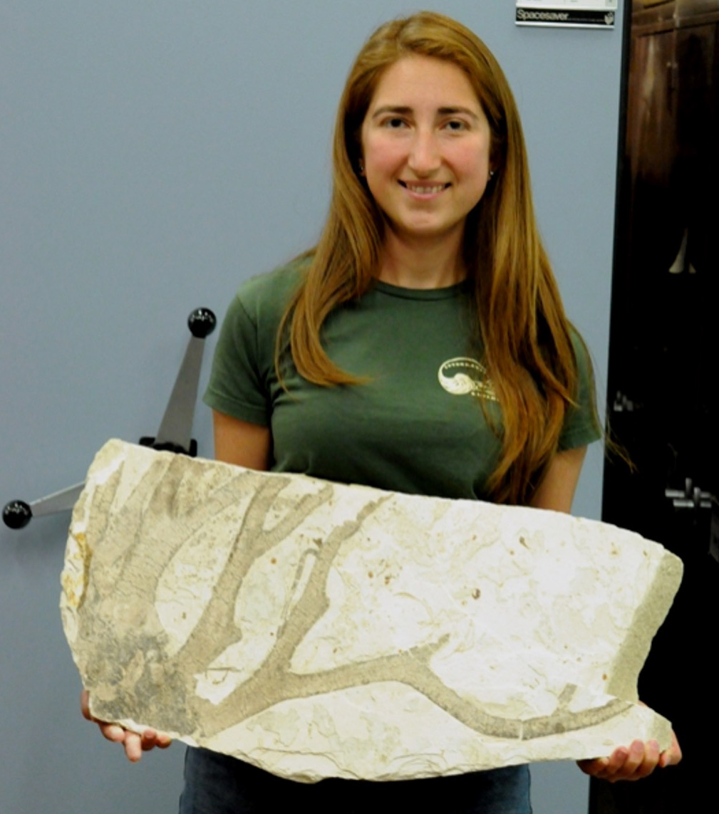 smiling young woman holding large slab of fossil kelp