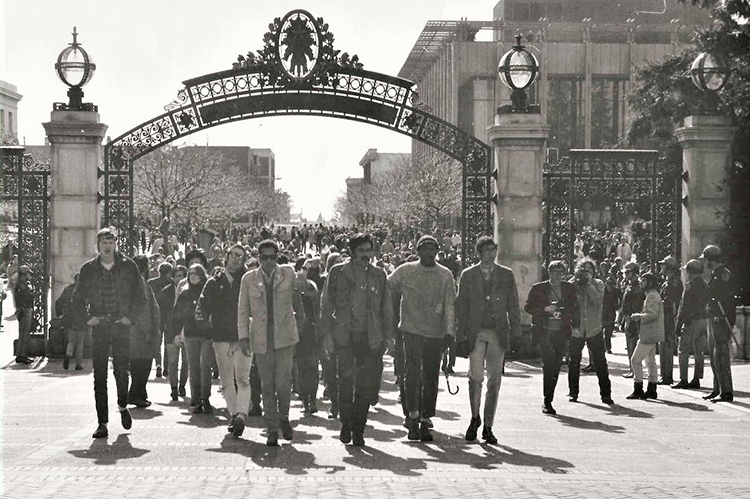 Black and white archival photo of Third World Liberation Front protesters walking out of the campus in front of Sather Gate.