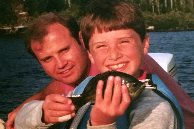 closeup of man and boy holding fish in canoe on lake