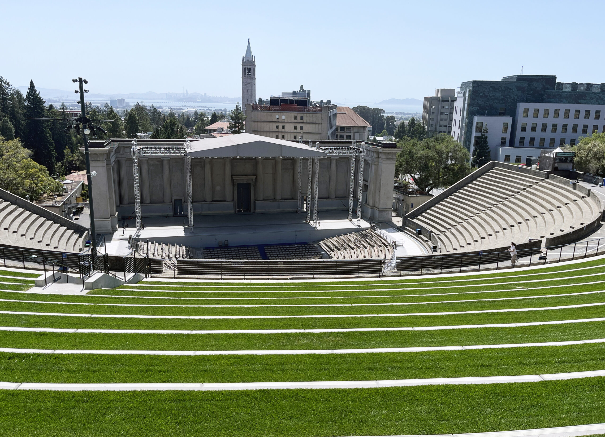 A view of the Greek Theatre stage from high above the U-shaped seating, where terraces have been built with green grass to allow for patrons to sit on the lawn and to contain concession stands.