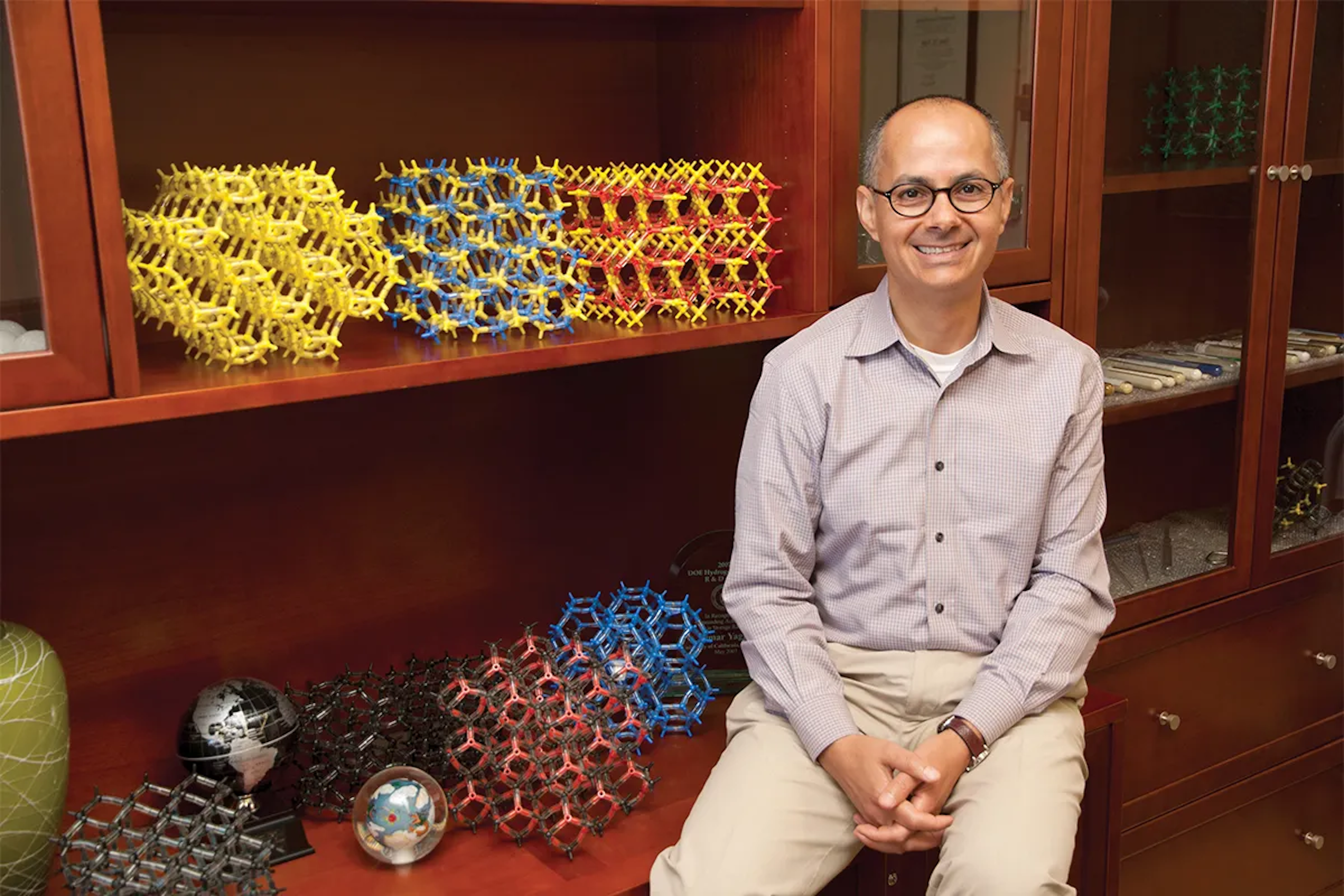 Omar Yaghi sits in front of a cabinet holding models of chemical structures in different colors