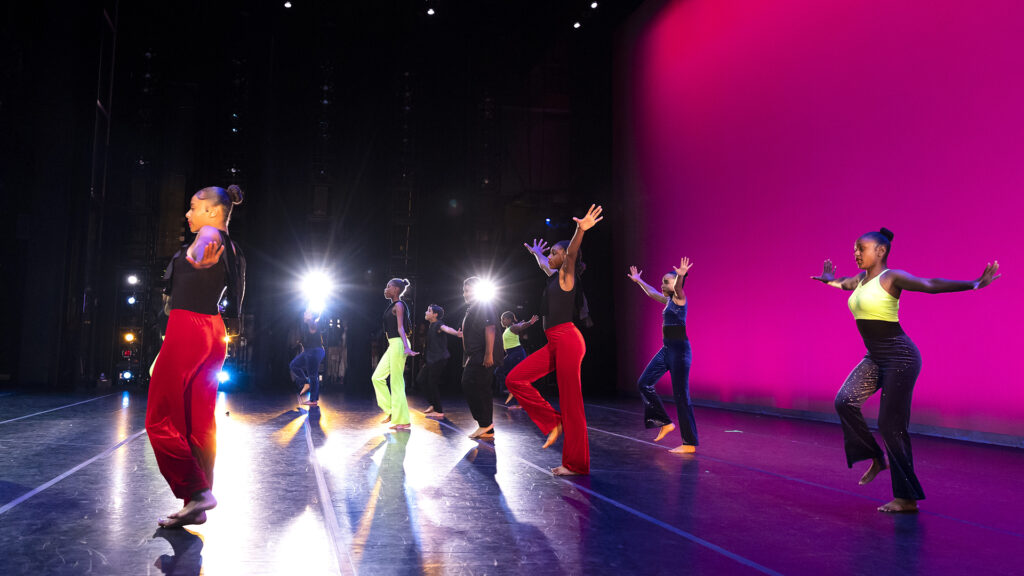 AileyCampers, dressed in bright clothes, give a final performance on stage with spotlights and a magenta wall behind them