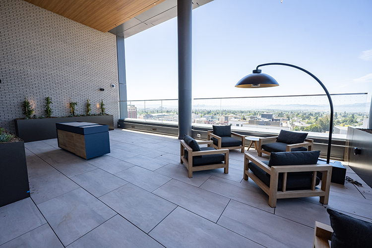 An outdoor terrace at Anchor House has sweeping views of the Golden Gate Bridge and San Francisco skyline, a tiled floor, plush armchairs, oversized lamps and planters.