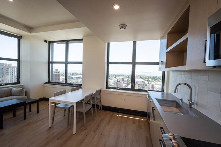 The kitchen and living room area in an apartment four four students has an open floor plan, a full kitchen with stainless steel appliances and large windows that provide an expansive view of the campus and Bay Area.