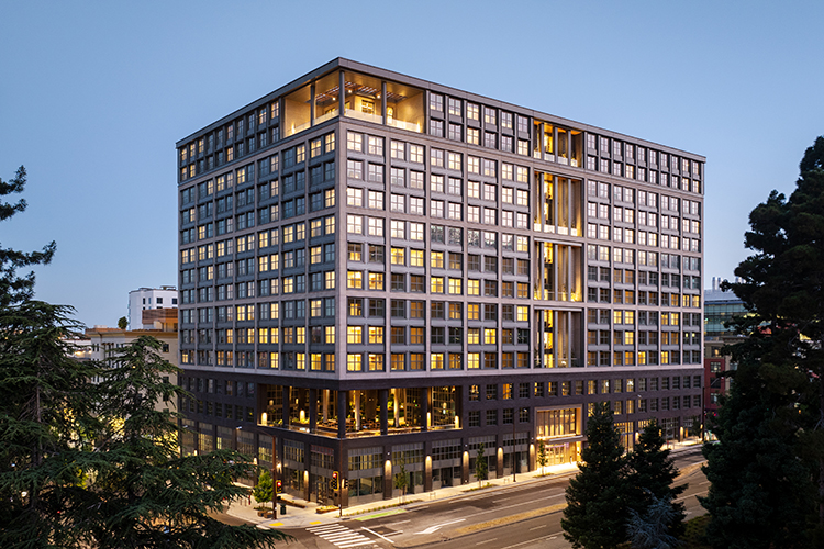 Anchor House, UC Berkeley's new residential building for transfer students, as seen at night from the West Crescent lawn. Its many windows and Oxford Street entrance are illuminated.