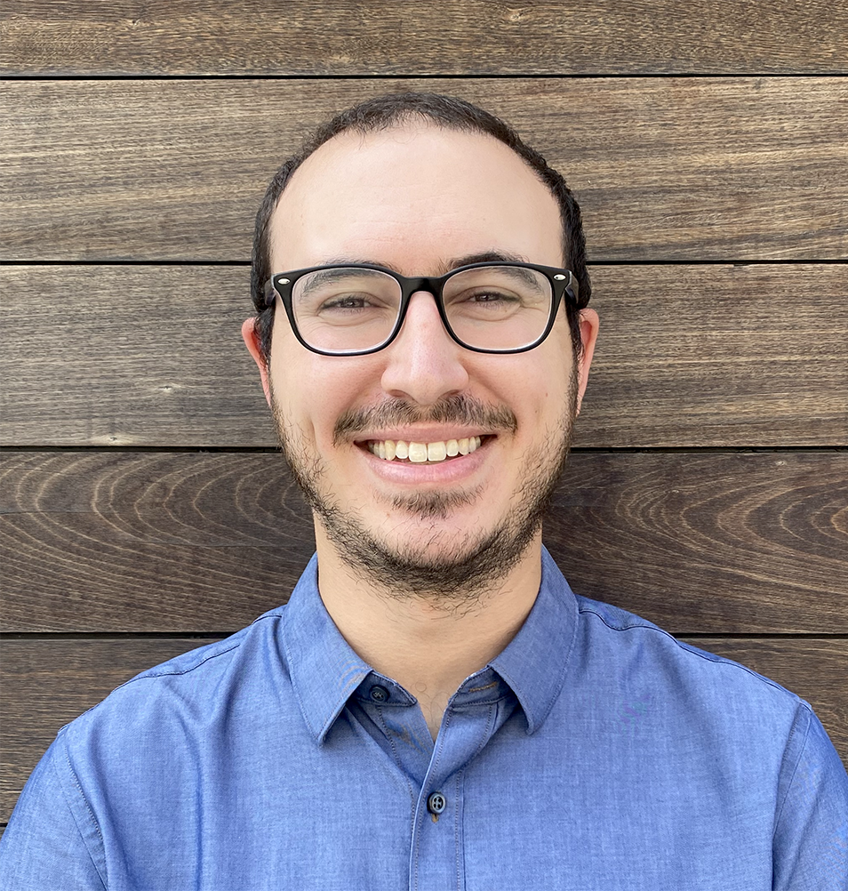 man in glasses and beard standing against a wooden fence