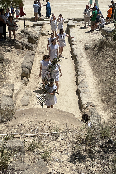 Barefoot young women, some of them Berkeley students, line up in white tunics outside an ancient entrance tunnel in Nemea, Greece, that leads to a stadium and track where they will compete in footraces as part of the 2024 Nemean Games. The Games took place in late June at a Berkeley archaeological excavation site in Greece where the campus has unearthed an early site of what today are the Olympic Games.