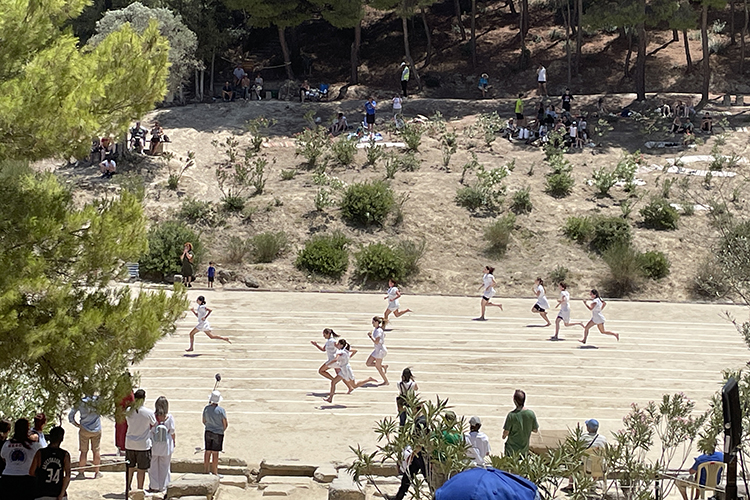 In late June 2024, people watch recreated footraces at Berkeley's archaeological excavation site in Ancient Nemea, Greece, while sitting on the slopes of the stadium using rugs and blankets.