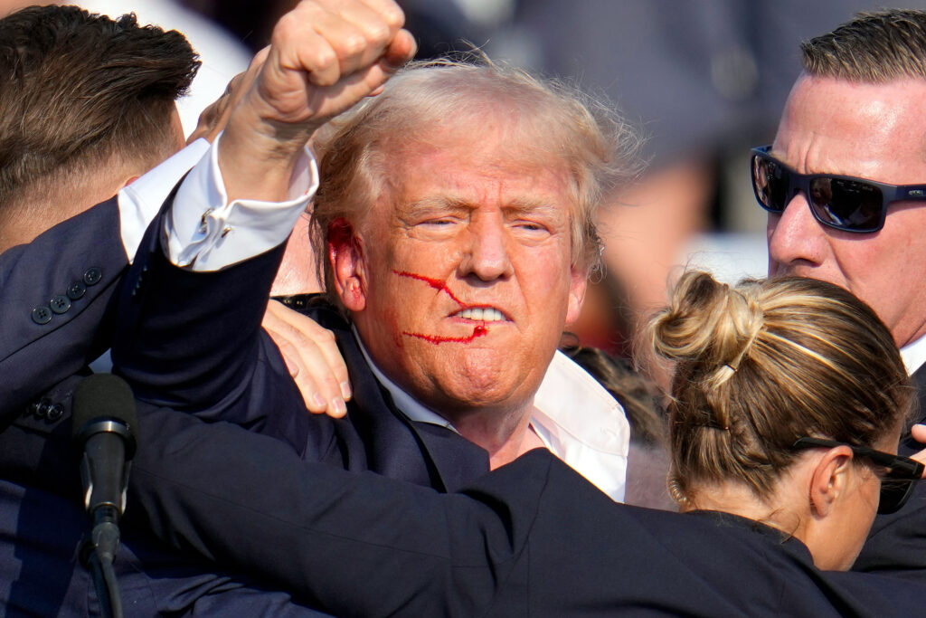 Donald Trump, with streams of blood trickling across his face, pumps his fist.