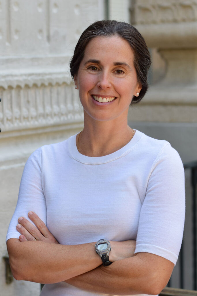 A portrait of Meredith Fowlie in front of a pillar with her arms crossed.