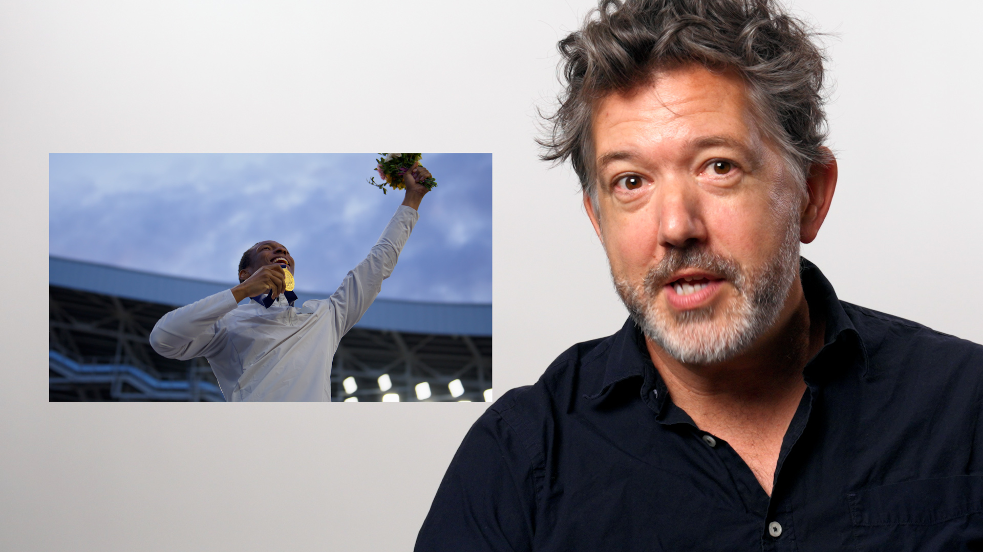 UC Berkeley musicology professor Nicholas Mathew sits for the camera, next to a still photo of an Olympian.