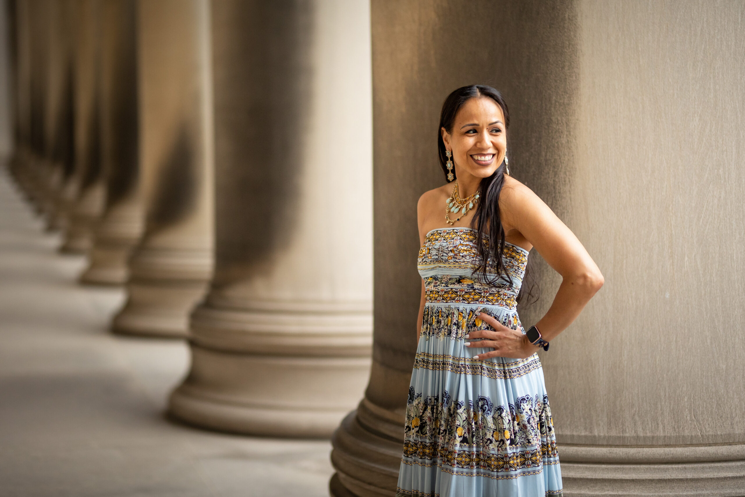 Dr. Gina Ann Garcia stands, smiling, in front of concrete columns wearing a vibrant patterned dress