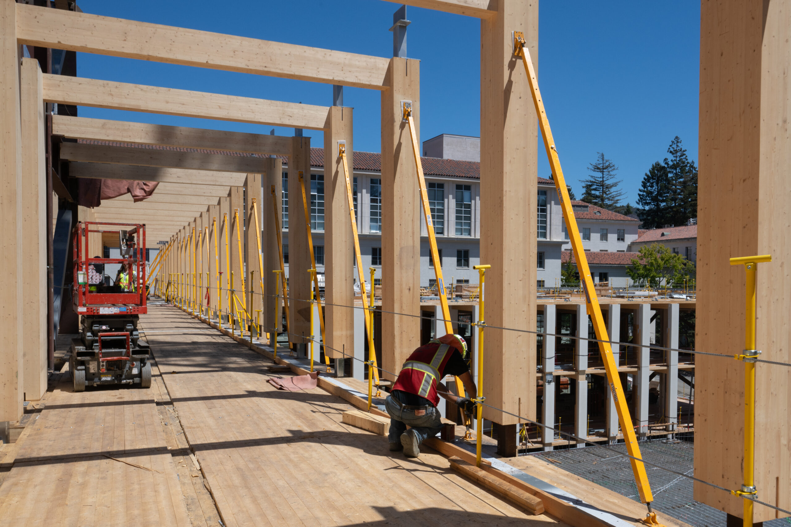 A worker kneels on an upper floor of the Undergraduate Academic Building, which is under construction, and works on a piece of mass timber, which is a material being used for the first time by the campus in construction. It's a lighter, safer and more energy-efficient alternative to traditional concrete-and-steel construction.