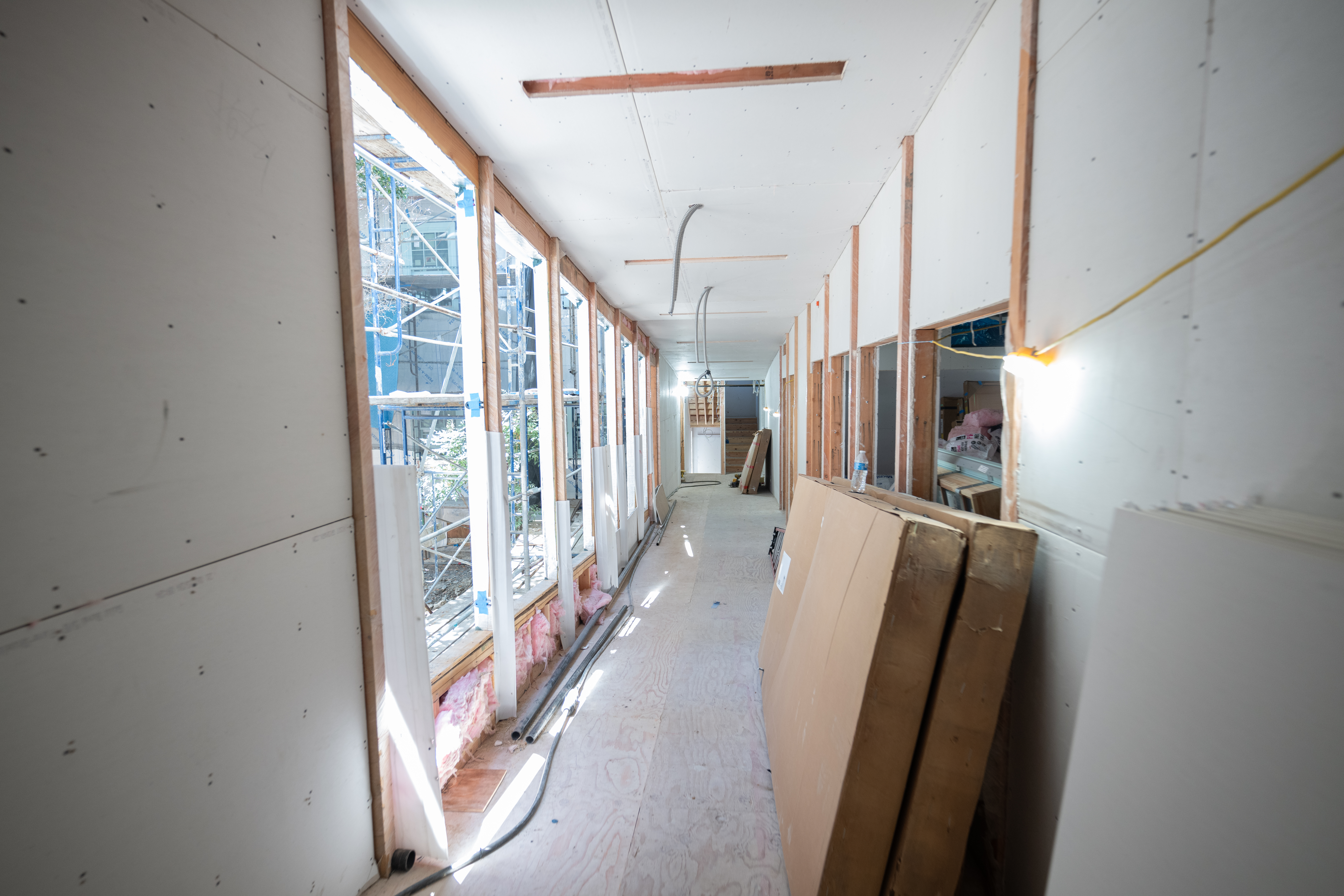 A long hallway in Creekside Center, a building under construction to create a new home for the Disabled Students' Program, is in an early stage of completion. The pink insulation under the windows is showing, and the hallway floor is plywood. Two large cardboard boxes sit unopened against the wall.