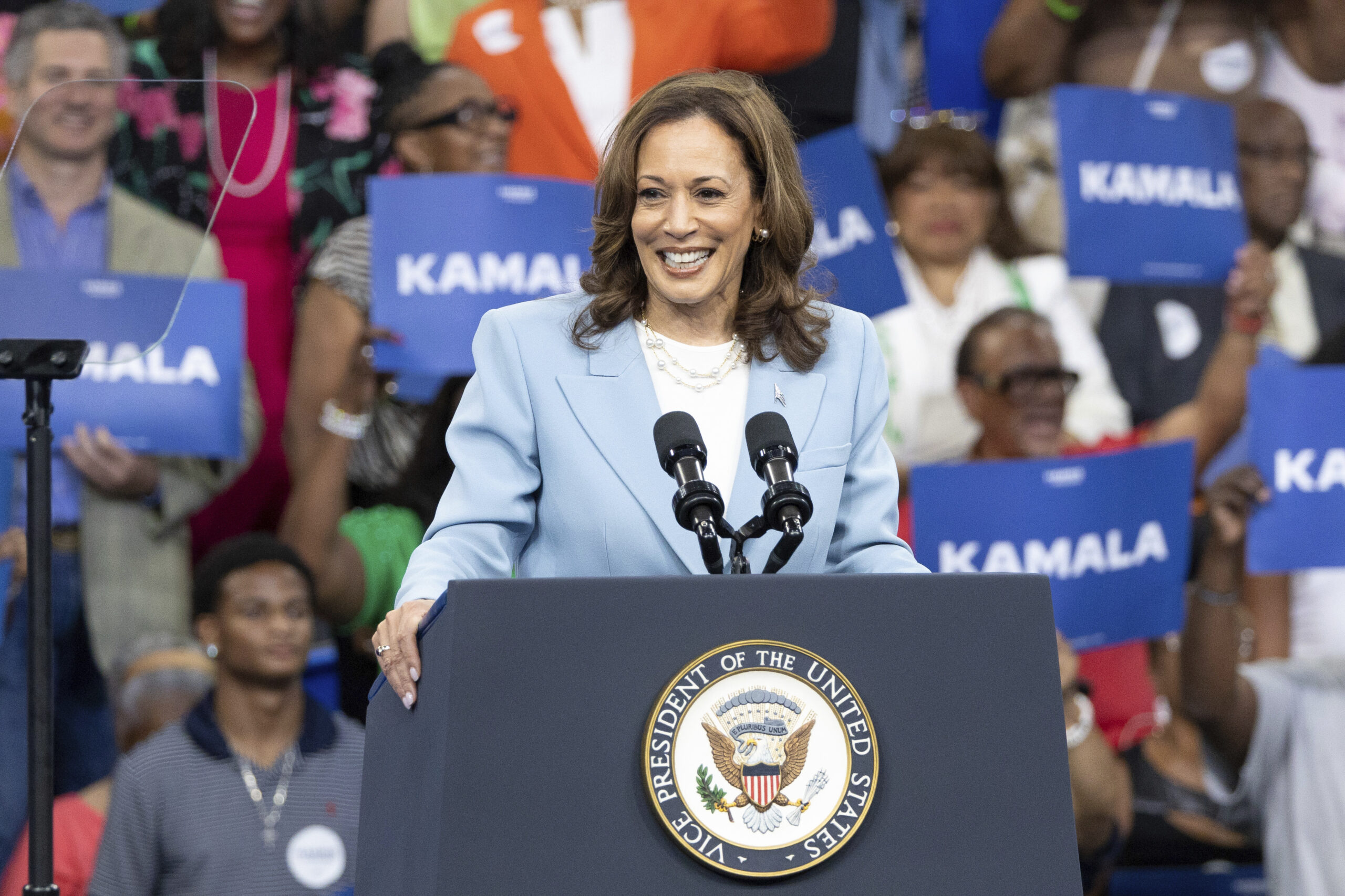 Kamala Harris speaking at a campaign rally in Atlanta, Georgia, with a crowd of people cheering behind her.