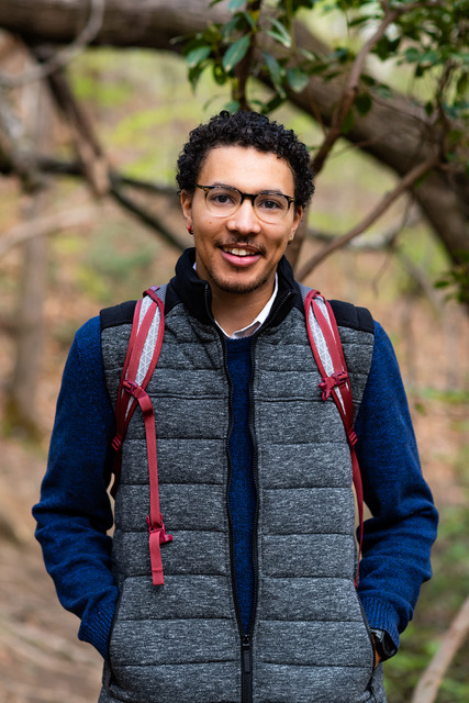 Tyus Williams stands in a forest and smiles at the camera.