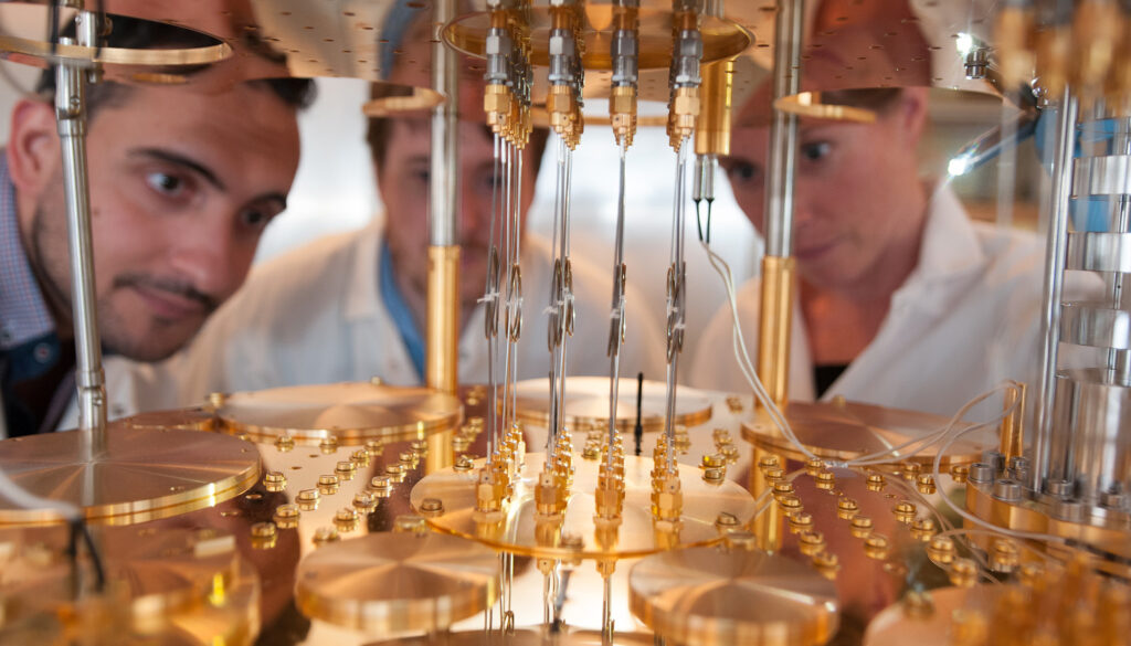 three people use a flashlight to peer into a scientific instrument