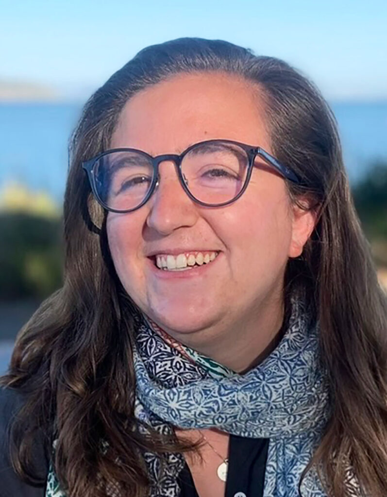 informal portrait of AJ Solovy, smiling, with a lake in the far background