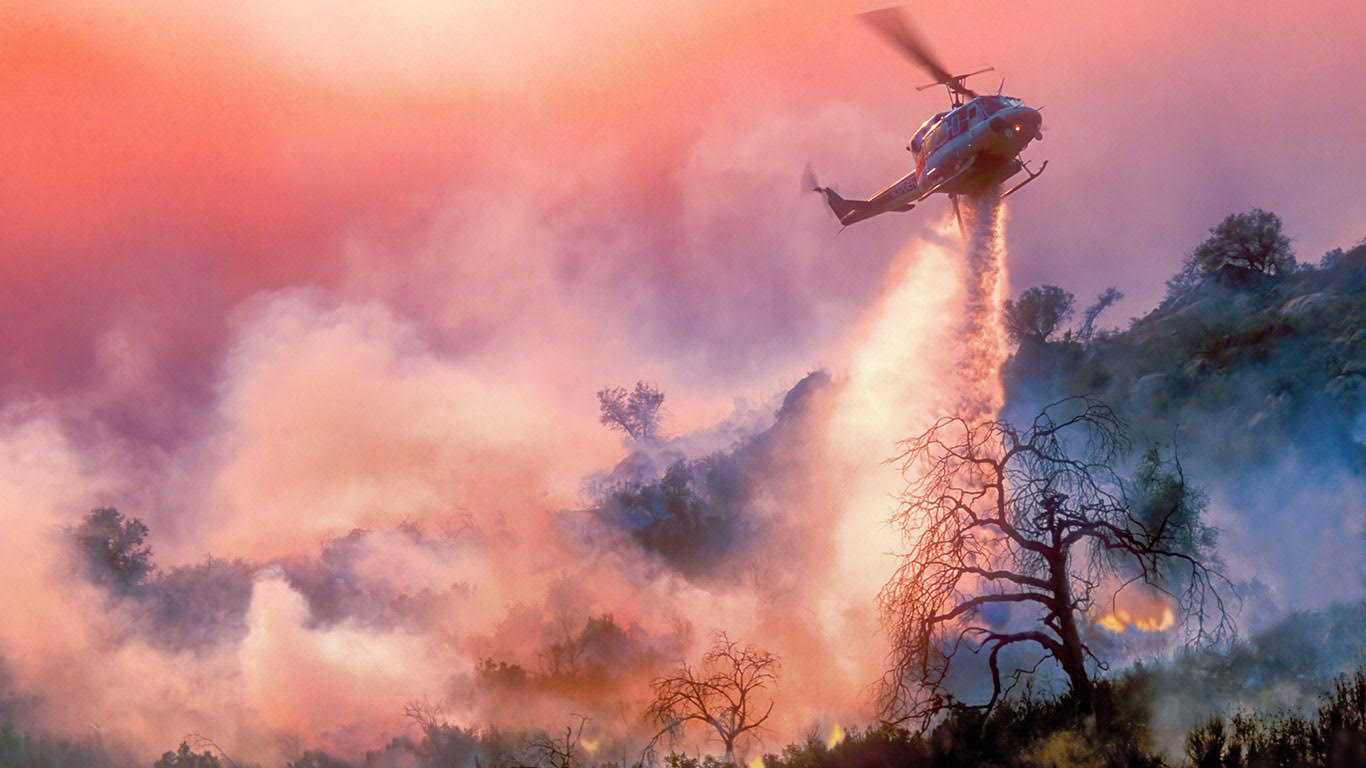 A helicopter drops a large amount of water onto a forest fire