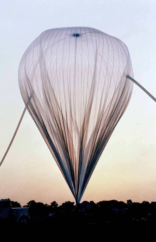 a tall, tethered balloon looms over trees at dawn