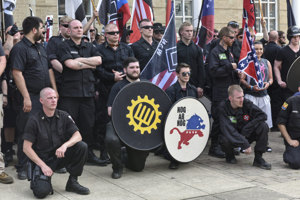 A group of men wearing black and holding confederate flags stand for a group photo outside of a brick building