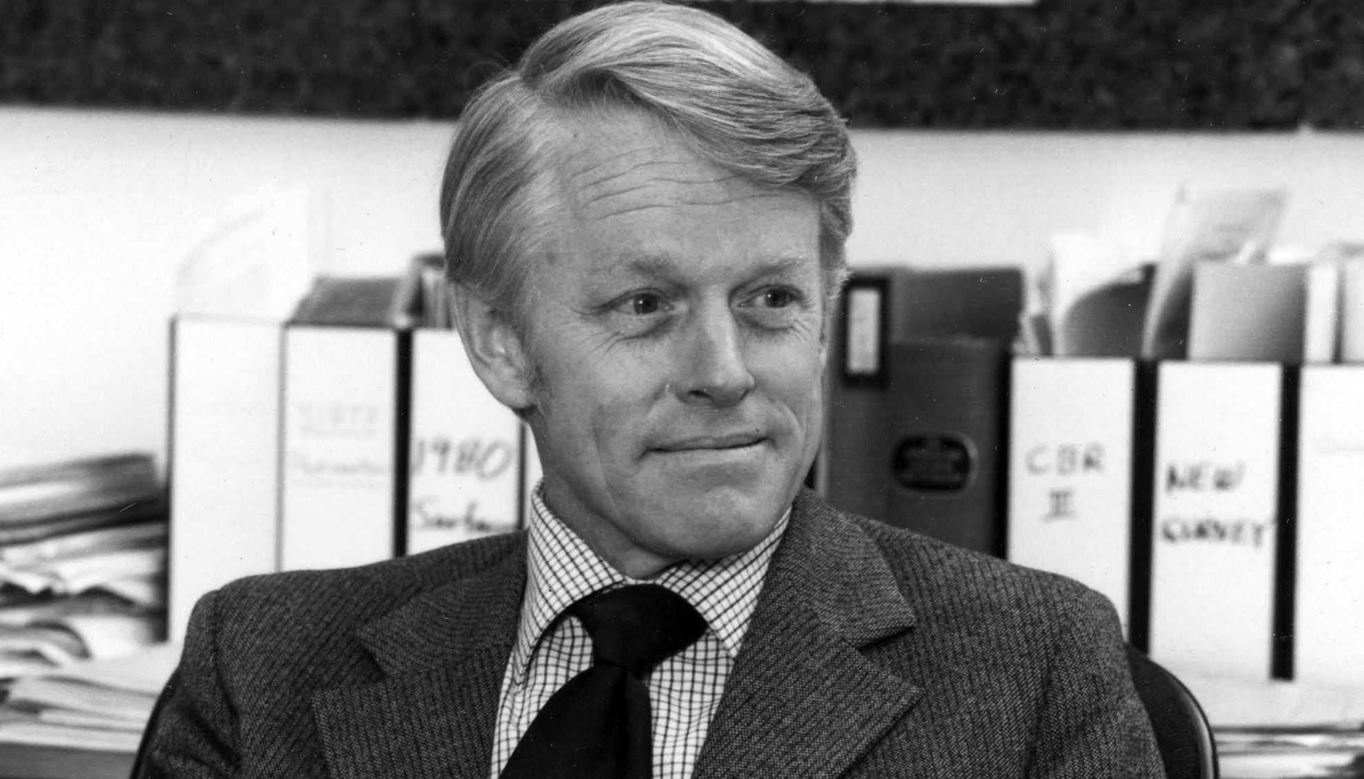 man seated in office wearing jacket and tie