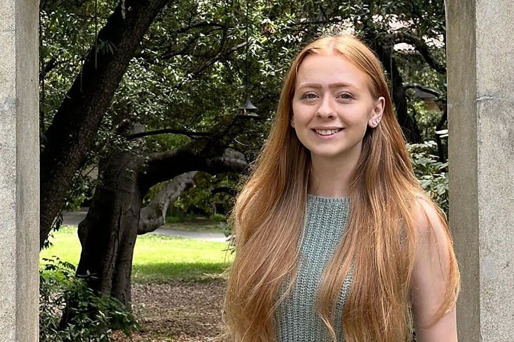 Informal portrait of Samantha Dalton, standing a stone door frame with trees in the background